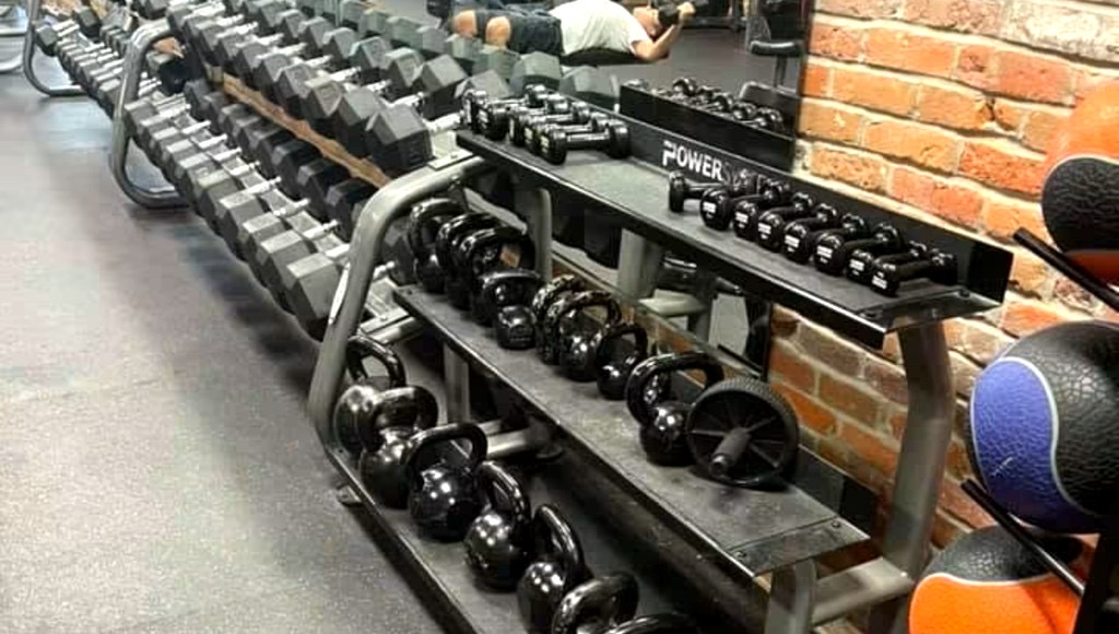 Free-weight floor with dumbbell rack, kettlebells and exposed brick wall.